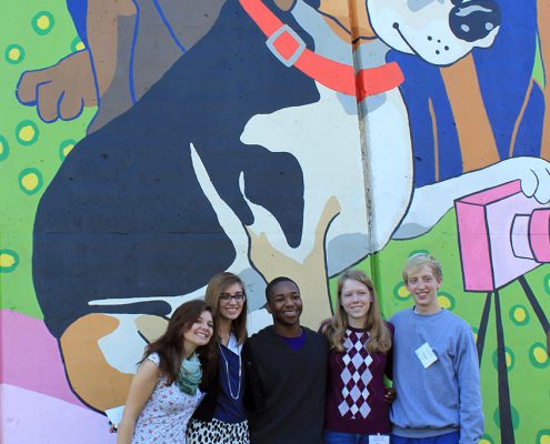 Friends pose for a photo in front of the Kellogg Park Dog Field mural by Artworks