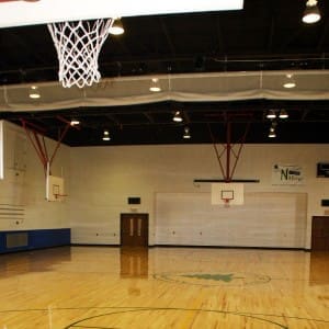 Basketball net in the foreground and view of volleyball curtain and two other basketball courts in the Anderson Parks RecPlex Gym