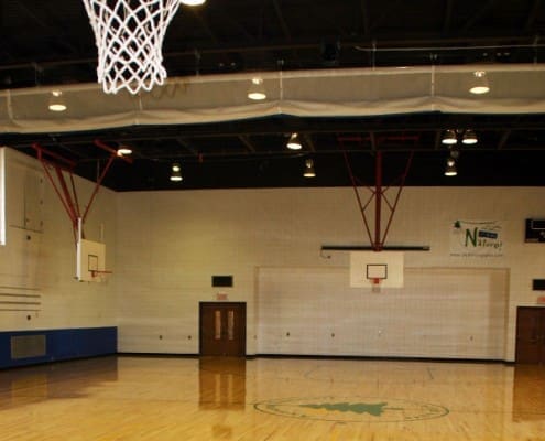 Basketball net in the foreground and view of volleyball curtain and two other basketball courts in the Anderson Parks RecPlex Gym