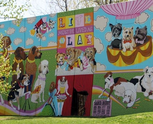 The vibrant Artworks mural at Kellogg Park Dog Field featuring various dog breeds. Text on the mural reads "Life must be lived as play" in colorful block letters.